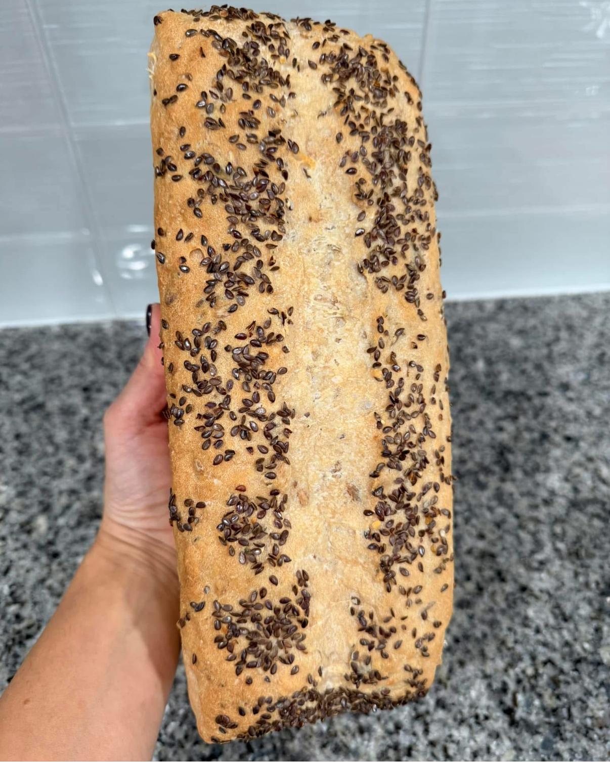 Fresh flax-topped gluten-free loaf held up to show its crust