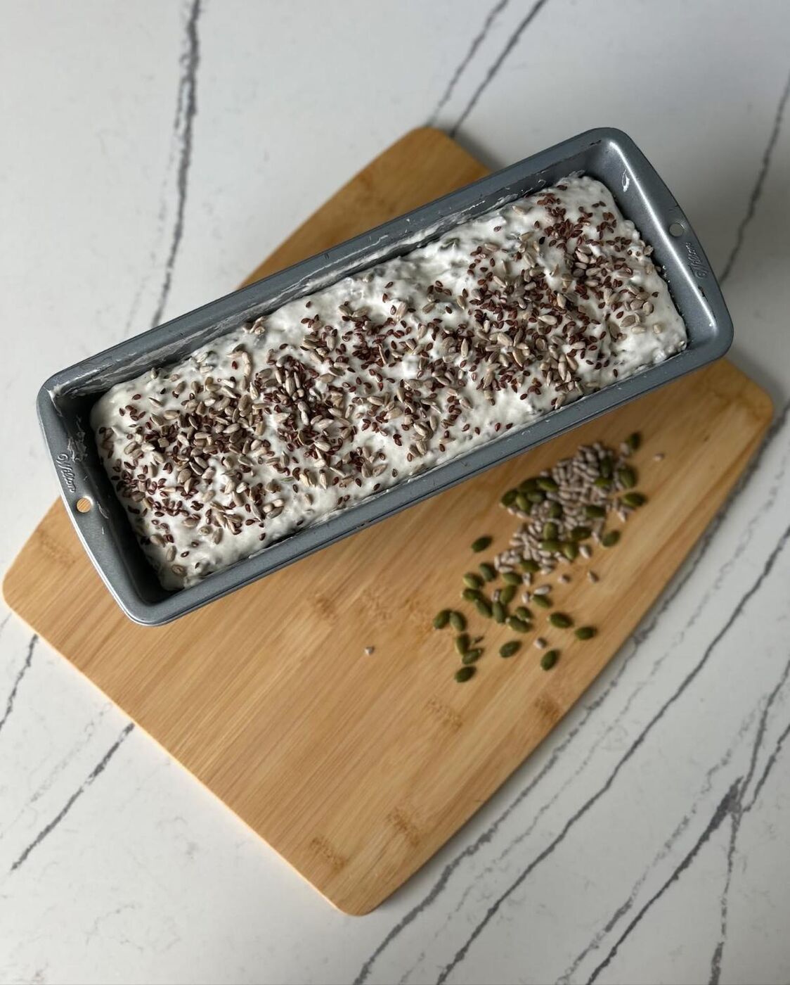 Seeded bread dough resting in a loaf pan
